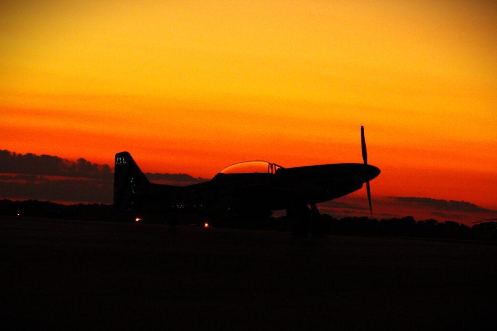 Small airplane sitting on ground with orange and yellow sunset in background